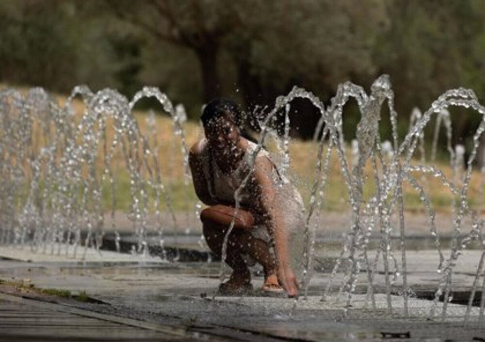 Imagen de una mujer refrescándose en una fuente